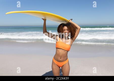 Mixed Race Frau hält ein Surfbrett am Strand Stockfoto