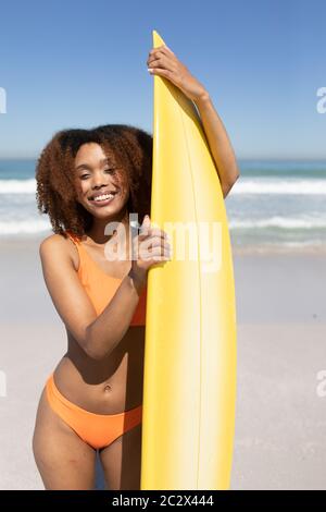 Mixed Race Frau hält ein Surfbrett am Strand Stockfoto