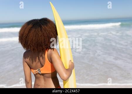 Mixed Race Frau hält ein Surfbrett am Strand Stockfoto