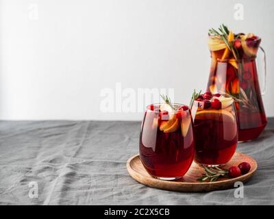 Wintersangria auf Tischplatte mit grauer Leinentischdecke. Juggly von Sangria und Gläser mit Obstscheibe, Cranberry und Rosmarin. Kopieren Sie den Bereich für den tex Stockfoto