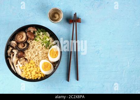 Ramen. Soba Nudeln mit Ei, Shiitake und Enoki-Pilzen, Mais und Schalotten, oben Schuss auf blauem Hintergrund mit Koteletts Stockfoto