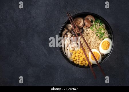Ramen. Soba Nudeln mit Ei, Shiitake und Enoki-Pilzen, Mais und Schalotten, von oben auf dunklem Grund mit c geschossen Stockfoto