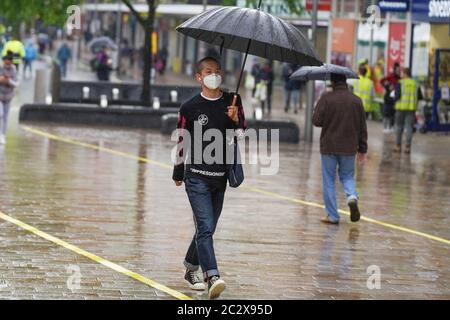 Sheffield, South Yorkshire . Wetter in Großbritannien; 18. Juni 2020. Ein Mann trägt eine Schutzmaske, während er sich während eines schweren Regenguß in Sheffield unter einem Regenschirm unterblättet.Bildnachweis: Ioannis Alexopoulos/Alamy Live News Stockfoto