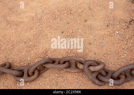 Rostige Ketten. Selektiver Fokus auf einem alten grossen rostigen Schiffe Ankerkette im Sand in der Nähe des Meeres mit großen kopieren. Zusammenfassung Hintergrund auf Sand. Stockfoto