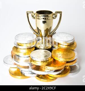 Ein Erfolg- oder Siegeskonzept mit einer Goldtrophäe oder einem Pokal, umgeben von Gold- und Silbermünzen in Form von Preisgeld Stockfoto