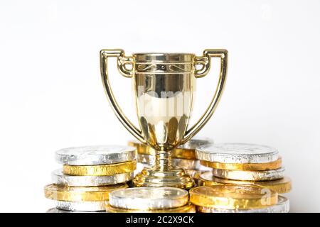 Ein Erfolg- oder Siegeskonzept mit einer Goldtrophäe oder einem Pokal, umgeben von Gold- und Silbermünzen in Form von Preisgeld Stockfoto