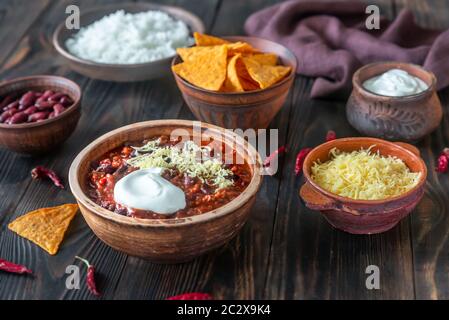 Schüssel mit Chili con carne mit Belag auf einem Holztisch Stockfoto