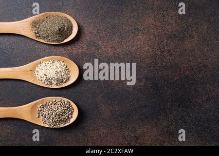 Hanfsamen, Mehl, Kerne in Löffeln auf dunklem Grund. Blick von oben. Stockfoto