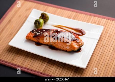 Japanische Küche inspirierte Speisen aus gegrilltem Lachsfilet in köstlicher Teriyaki-Sauce (Sojasauce Basis) und Rosenkohl auf weißem Teller glasiert. Stockfoto