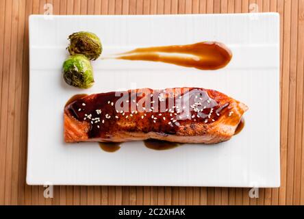 Japanische Küche inspirierte Speisen aus gegrilltem Lachsfilet in köstlicher Teriyaki-Sauce (Sojasauce Basis) und Rosenkohl auf weißem Teller glasiert. Stockfoto