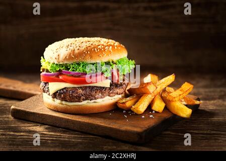 Lecker Hamburger mit Käse und Pommes frites auf Holztisch und dunklen Hintergrund Stockfoto