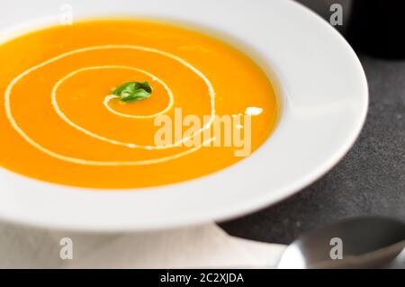 Kürbissuppe mit Sahne wirbeln. Squashsuppe wird traditionell während der Herbstsaison gegessen. Kürbis oder Butternusskürbis werden mit anderem Gemüse gemischt Stockfoto