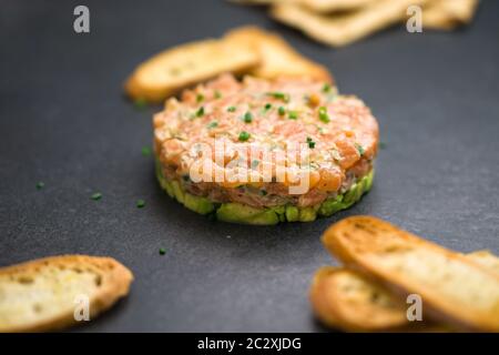 Klassische Lachstartare wird mit gehacktem frischen rohen Lachsfischen, Avocado, Tatarsauce und Crackern oder Brot hergestellt. Gesunde Vorspeise Gericht. Stockfoto