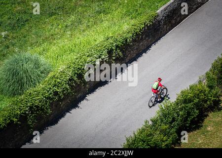 Der Radfahrer fährt mit dem Mountainbike mit voller Federung entlang einer Asphaltstraße entlang der grünen Plantagen hinauf. In Samt gekleidet Stockfoto