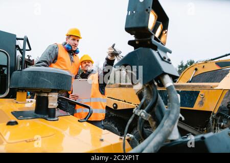 Zwei männliche Arbeiter auf Bagger im Grabenbetrieb oder Steinbruch auf Maschinen abgebildet Stockfoto