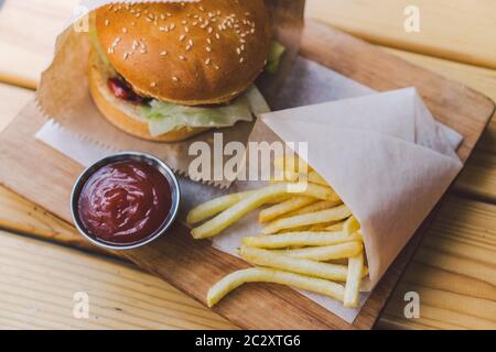 Frische leckere Burger und pommes auf Holztisch. pommes und bbq-Sauce auf Holzplatte. Street Food Burger und gebratene Pota Stockfoto