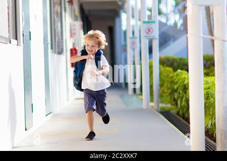 Kind, das zur Schule geht. Junge läuft in Schulhof. Kleine Schülerin freut sich, wieder in die Vorschule oder den Kindergarten. Beginn der Klasse nach dem Urlaub. Stockfoto