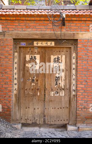 Bild eines Paares alter Holztüren in einem Ziegelhaus, in der alten Stadt Zhou Cun, Provinz Shandong, China. Vertikale Ausrichtung. Stockfoto