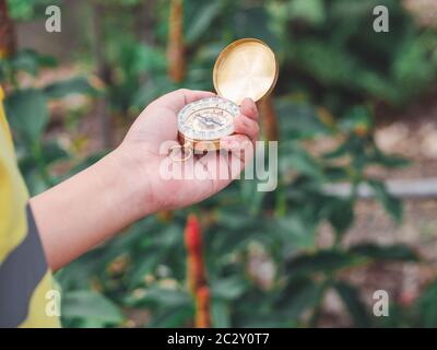 Hand von Kind Hand mit magnetischen goldenen Kompass während der Reise im Dschungel oder Wald und auf der Suche nach einem Abenteuer Route zu Berg oder Hügel. Episch Stockfoto