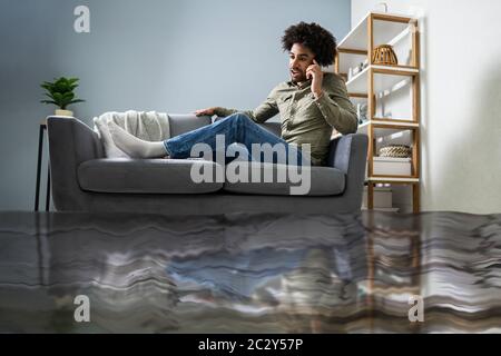 Überschwemmt von Wasser Leckage Vor Mann sitzt auf einem Sofa zu Klempner Stockfoto