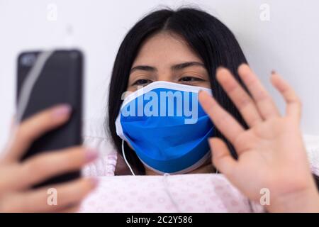 Frau nutzt ihr Handy, um einen Videoanruf zu tätigen, während sie zu Hause wegen Coronavirus-Quarantäne ist Stockfoto