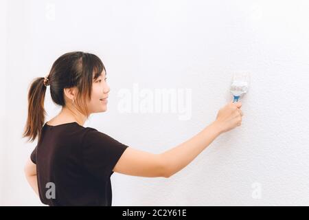 Glückliche asiatische Frau malen die Wand ihres neuen Hauses Stockfoto