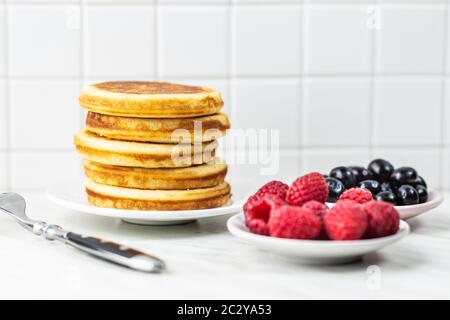Süße hausgemachte Pfannkuchen mit Blaubeeren und Himbeeren auf weißem Tisch. Stockfoto
