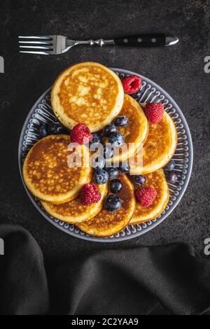 Süße hausgemachte Pfannkuchen mit Blaubeeren und Himbeeren auf dem alten Küchentisch. Stockfoto