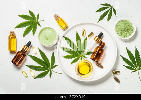 Cannabisöl und grüne Blätter am weißen Tisch. Stockfoto