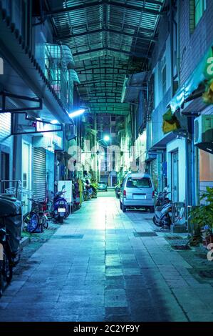 Leere und dunkle Gasse in Taipei, Taiwan. Die kleine Straße in einem Wohnviertel wird nachts von blauen Straßenlaternen beleuchtet Stockfoto