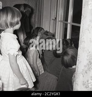 1960, historische, aufgeregt kleine Kinder auf einer Party in einem Haus aus dem Fenster schauen, um die Überraschung zu sehen, England, Großbritannien. Stockfoto