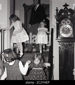 1960er, historische, aufgeregt junge Kinder auf einer Party gehen eine Treppe neben einer großen Großvater Uhr, England, Großbritannien. Stockfoto