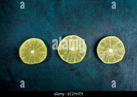 Drei reife frische, saftige geschnittene Limettenscheiben werden auf smaragdgrünem Hintergrund in Reihe gelegt. Limette ist Zutat für erfrischende Mojito trinken. Draufsicht, Kopieren Stockfoto