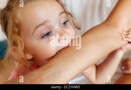 Kleinkind weiblichen beißen den Arm der Mutter. Kinder Gesicht Phasen des Wachstums, einschließlich Beißen. Stockfoto