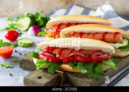 Fast Food. Hot Dog mit Grillwurst und frischem Gemüse auf einem hellen Stein- oder Schiefertisch. Stockfoto