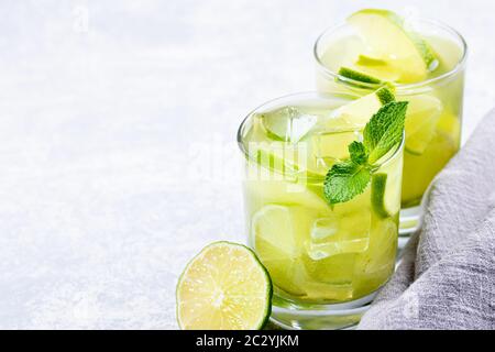 Zwei Gläser eisgrüner Matcha-Tee mit Limette, Eis, frischer Minze und grauer Serviette auf hellgrauem Hintergrund. Gesundes erfrischendes Getränk reich an antiox Stockfoto