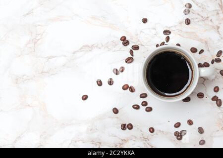 Weiße Kaffeetasse gefüllt mit Kaffee und Kaffeebohnen auf Marmorhintergrund, Draufsicht Stockfoto