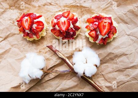 Schöne kleine Kuchen mit Erdbeeren zusammen mit einem Zweig der Baumwolle liegt auf Kraftpapier. Stockfoto