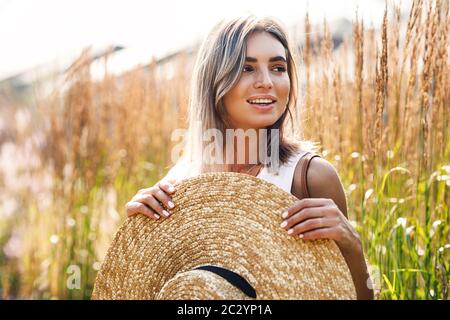Junge schöne Frau mit einem großen Strohhut auf einem Feld, umgeben von hohem Gras Stockfoto