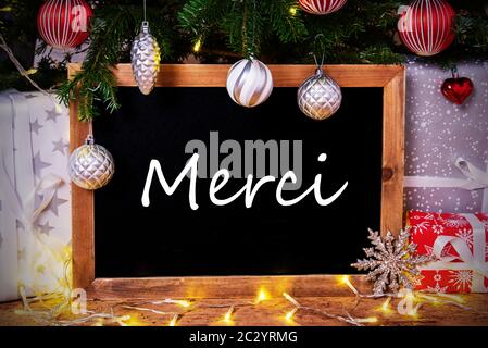 Tafel mit französischen Text Merci bedeutet. Vielen Dank. Weihnachtsbaum mit Kugel, Geschenke und Lichterketten Stockfoto