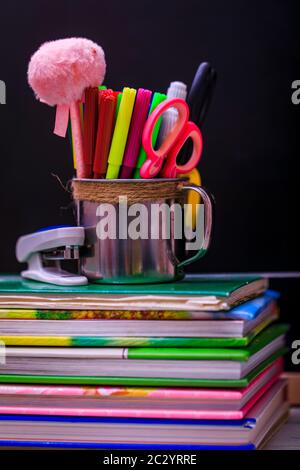Bücher, Apfel, Stifte und Stifte auf Holztisch, vor dem Hintergrund einer Kreidetafel. Konzept für den Tag des Lehrers, Kopierraum. Stockfoto