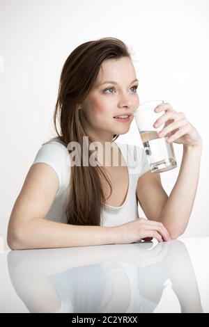 Hübsche, junge Frau in ihrer modernen, sauberen und hellen Küche, die sich selbst gießt und ein Glas kaltes Leitungswasser trinkt (farbige Bildstelle; flacher Freiheitsgrad) Stockfoto