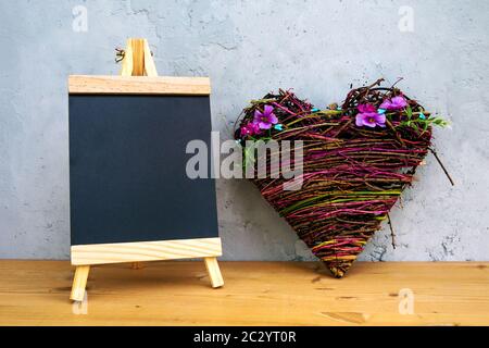 Kleine Tafel und Herzform mit Blumen auf Holztisch mit grauem Hintergrund Stockfoto