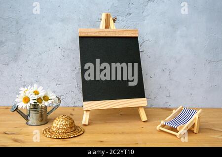 Kleine Tafel mit Miniatur-Gießkanne, Liege und Strohhut auf Holztisch Stockfoto