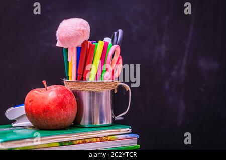 Bücher, Apfel, Stifte und Stifte auf Holztisch, vor dem Hintergrund einer Kreidetafel. Konzept für den Tag des Lehrers, Kopierraum. Stockfoto