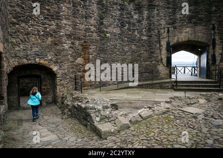 Eine weibliche Touristin spaziert über den felsigen Fuß des Blackness Castle, geformt wie ein Schiff, während sie Filmorte des beliebten Zeitfahrens Outlander tv besucht Stockfoto