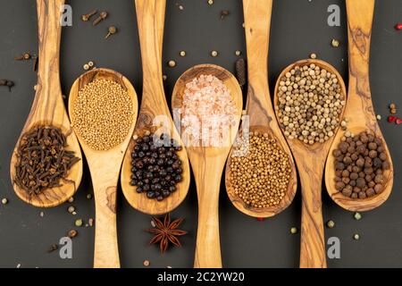 Gewürz und Essen - Hintergrund aus verschiedenen Gewürzen in Kochlöffeln aus olivem Holz auf schwarzem Grund Stockfoto