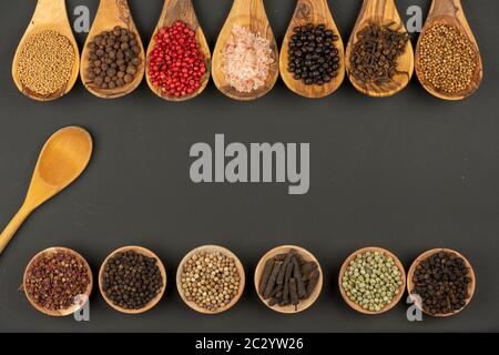 Sieben Kochlöffel aus olivem Holz in einer Reihe und sechs kleine Holzschüsseln in einer Reihe mit verschiedenen Gewürzen und einem Holzkochlöffel auf einem Schwarz Stockfoto