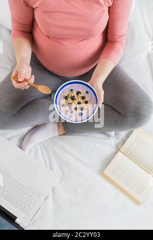 Blick auf junge Frauen, die Müsli essen und einen Laptop im Bett benutzen, neben dem Konzept für ein gesundes Frühstück Stockfoto