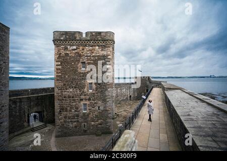 Eine schöne Frau trägt einen warmen weißen Pelz-Kragen Mantel und Wollhut geht den Balkon mit Blick auf Blackness Castle geformt wie ein Schiff, während V Stockfoto